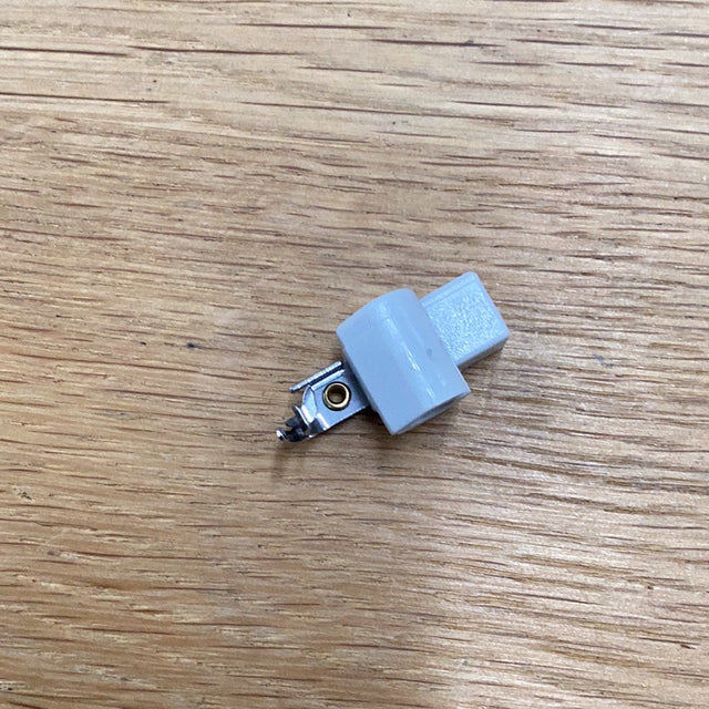 Brother XC3568151 replacement needle-threader hook, angled view of the grey holder and metal hook on a wooden surface.