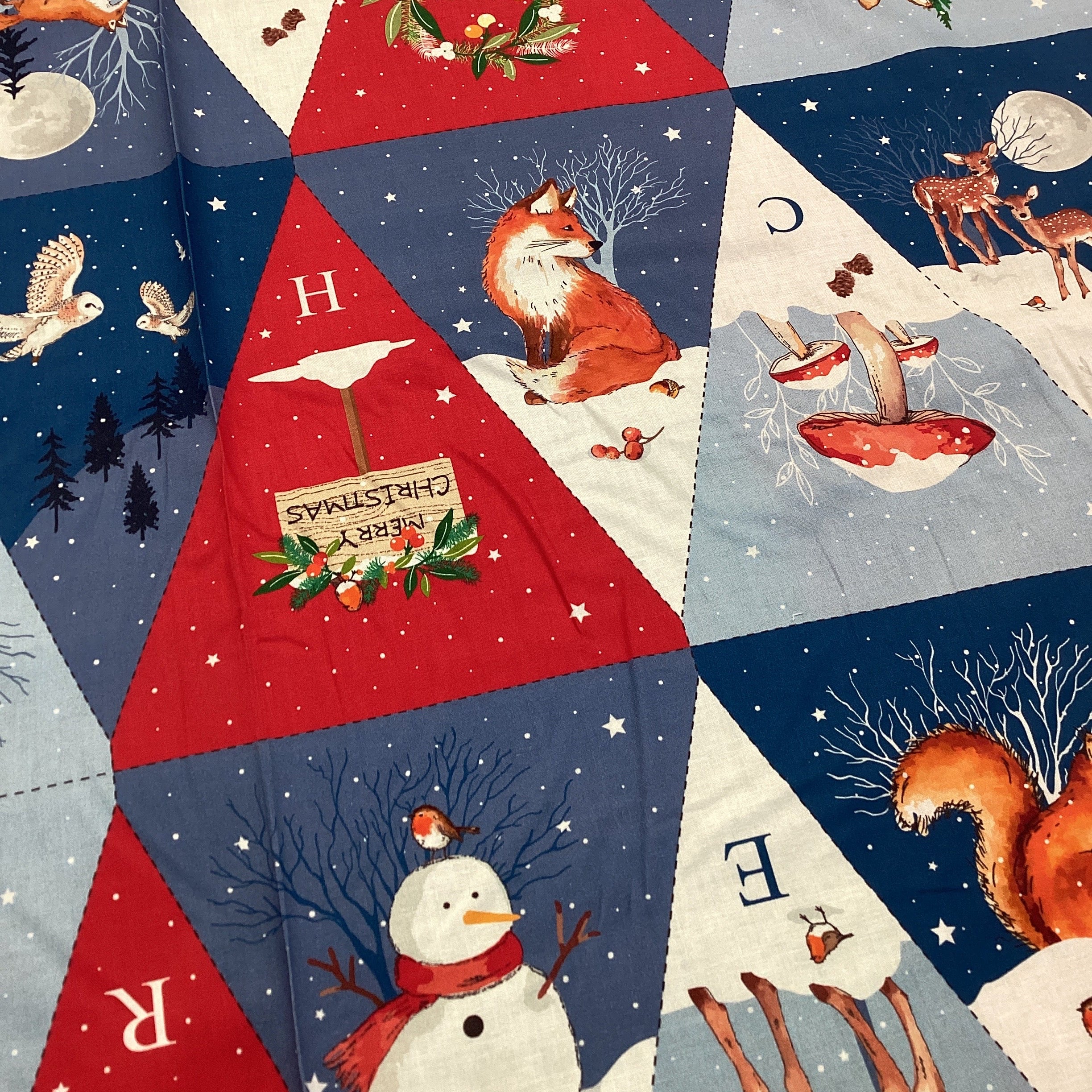 Christmas-themed fabric with reindeer, fox, snowman, and festive text on a patchwork pattern.